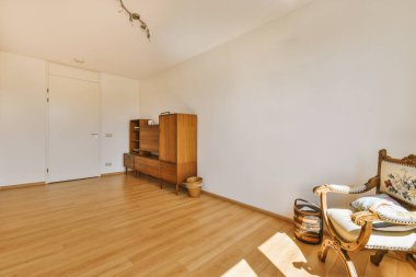 Modern dolap ve klasik sandık, beyaz duvarları ve ahşap zemini olan geniş bir odada, kapıların ve hasır sepetin yanına yerleştirildi.