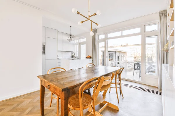 Interior of spacious light dining room with elegant chandelier located near kitchen with comfortable furniture and appliances