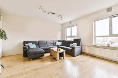 Televizyonun önündeki gri kanepe ve pencerenin karşısındaki yemek masası ile aydınlık oturma odasının basit bir iç mekanı.