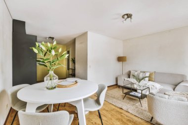 Konforlu kanepe döşenmiş oturma odasının rahat iç tasarımı ve modern tavan arası dairesinin beyaz duvarları ve sütunlarıyla döşenmiş ahşap masa.