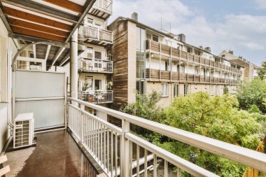 Narrow brick balcony with metal railings, wooden chair and door