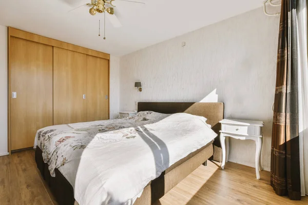 Stock image Home interior design of bedroom with bed and wooden wardrobe placed in corner near window in modern apartment