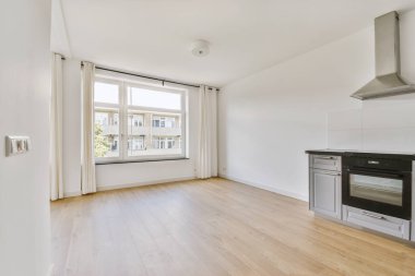 Pencereleri ve ahşap parke zemini olan boş beyaz mutfağın içi.