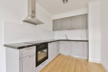 Pencereleri ve ahşap parke zemini olan boş beyaz mutfağın içi.