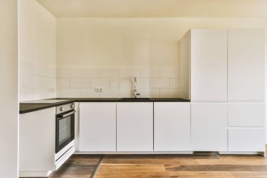 Pencereleri ve ahşap parke zemini olan boş beyaz mutfağın içi.