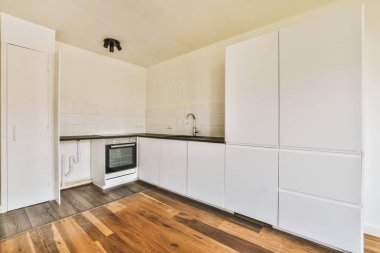 Pencereleri ve ahşap parke zemini olan boş beyaz mutfağın içi.