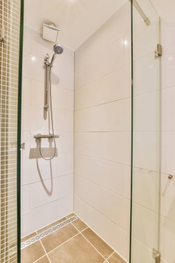 Çağdaş dairenin küçük fayanslı banyosunda lavabo ve duş arasında bulunan sifon tuvaleti