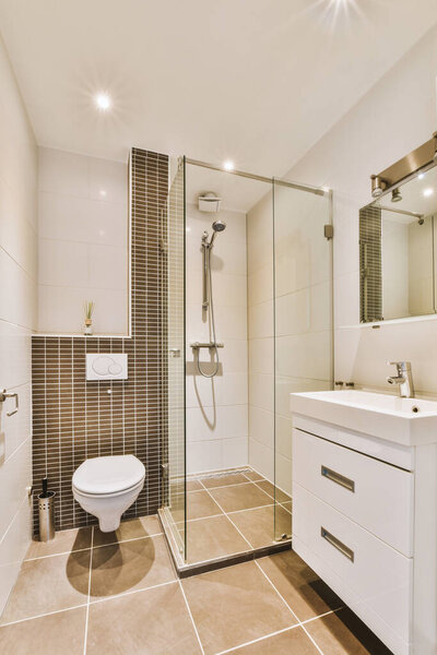 Flush toilet located between sink and shower in small tiled bathroom of contemporary apartment