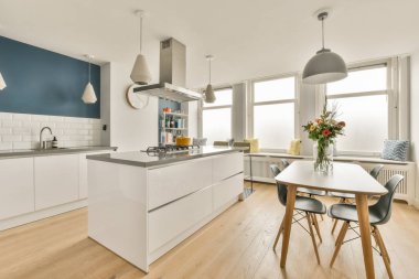 Çağdaş dairenin geniş odasındaki dinlenme odası ve mutfağın yakınındaki sandalyeli ve çiçekli masa.