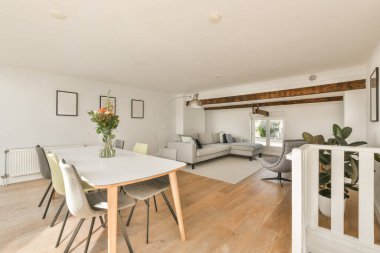 Çağdaş dairenin geniş odasındaki dinlenme odası ve mutfağın yakınındaki sandalyeli ve çiçekli masa.