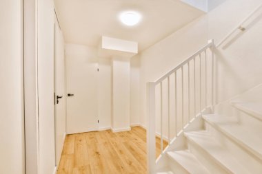 Minimalist iç tasarımı olan modern lüks dairenin ikinci katına çıkan ahşap merdivenli beyaz koridor.