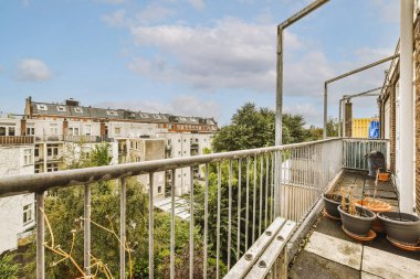 Metal parmaklıklı dar tuğla balkon, tahta sandalye ve camlı kapı mutfağa açılıyor.