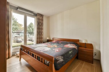 Yatak örtüleri ve yatak odasındaki aydınlık yatak odasının penceresinin yanına konmuş lambasıyla rahat bir yatak.