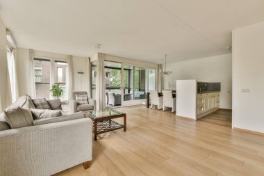 Çağdaş dairenin geniş odasındaki dinlenme odası ve mutfağın yakınındaki sandalyeli ve çiçekli masa.