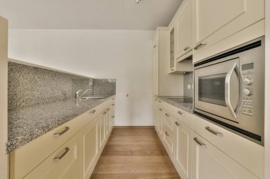 Gündüz vakti modern bir dairede yemek odasının yakınında modern dolaplar ve aletlerle donatılmış aydınlık mutfağın içi.