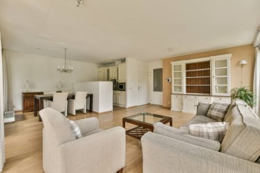 Çağdaş dairenin geniş odasındaki dinlenme odası ve mutfağın yakınındaki sandalyeli ve çiçekli masa.