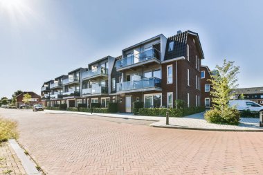 Arabaları, ağaçları ve fenerleri olan boş bir kaldırımdan panorama manzaralı evler.