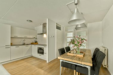 Çağdaş dairenin geniş odasındaki dinlenme odası ve mutfağın yakınındaki sandalyeli ve çiçekli masa.