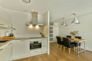 Çağdaş dairenin geniş odasındaki dinlenme odası ve mutfağın yakınındaki sandalyeli ve çiçekli masa.