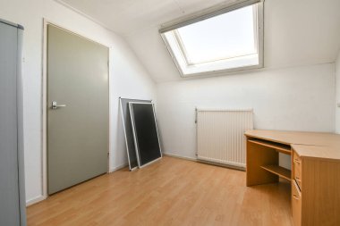 Döşemeleri parke kaplı, beyaz duvarları masa ve radyatörle döşenmiş kasvetli oda.