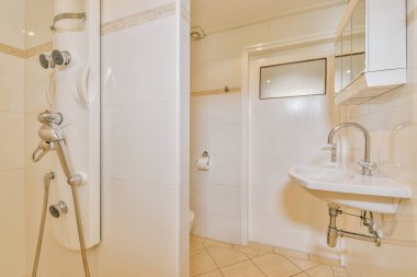 Çağdaş dairenin küçük fayanslı banyosunda lavabo ve duş arasında bulunan sifon tuvaleti