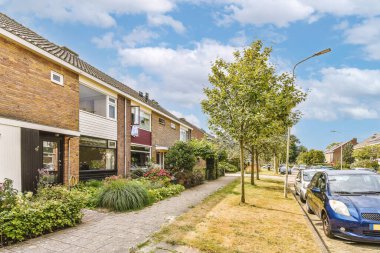 Arabaları, ağaçları ve fenerleri olan boş bir kaldırımdan panorama manzaralı evler.