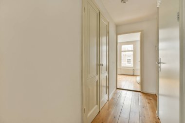 Işık koridoru, giriş kapısı olan iki katlı bir apartman dairesi. Minimalist ahşap merdivenler, gün ışığında üst kata çıkıyor.