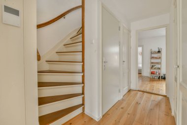 Işık koridoru, giriş kapısı olan iki katlı bir apartman dairesi. Minimalist ahşap merdivenler, gün ışığında üst kata çıkıyor.