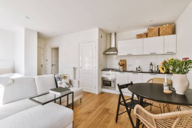 Günümüz minimalist tasarımı. Hafif stüdyo dairesinin ahşap masası ve oturma odası ile beyaz duvarları ve parke zemini arasında yemek masası ve sandalyeleri var.