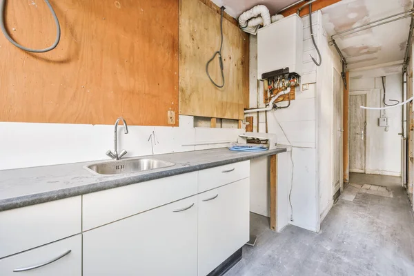 stock image Fragment of interior of light narrow home kitchen with minimalist style white furniture with sink and stove