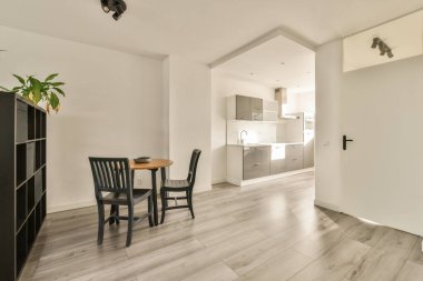 Çağdaş dairenin geniş odasındaki dinlenme odası ve mutfağın yakınındaki sandalyeli ve çiçekli masa.