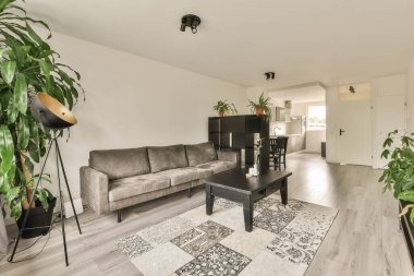 Çağdaş dairenin geniş odasındaki dinlenme odası ve mutfağın yakınındaki sandalyeli ve çiçekli masa.