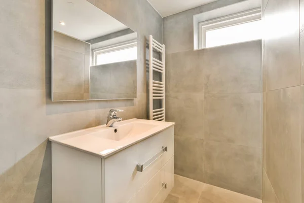 Shelves with towels and drying rack located near sinks with mirrors and bathtub in light bathroom of modern apartment