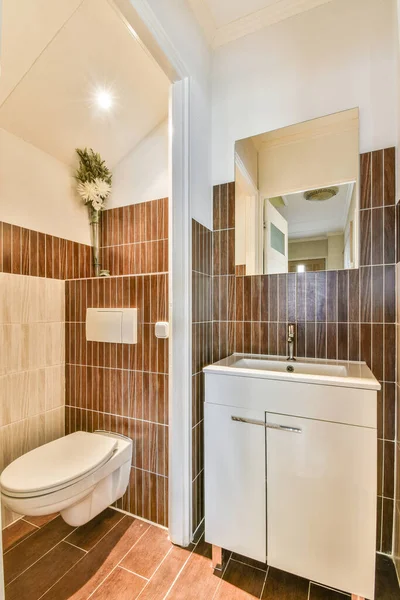 家の小さなトイレに茶色のタイル張りの壁に設置された居心地の良いトイレとセラミックシンク — ストック写真