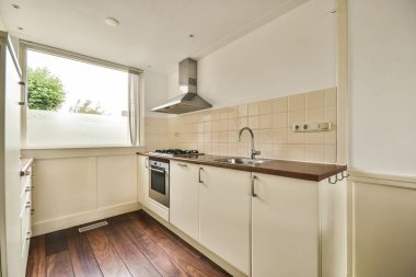 Pencerenin altında lavabo ve sobalı hafif mobilyalar olan iyi organize edilmiş küçük bir ev mutfağı.