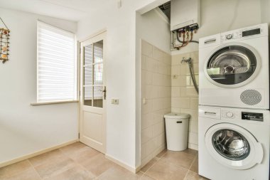 Beyaz duvarları ve koyu renk döşemeleri olan modern, parlak çamaşır odasının içi.