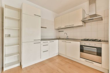 Pencereleri ve ahşap parke zemini olan beyaz mutfağın içi.