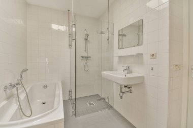 Aynalı lavabo ve temiz küvet modern banyoda cam kapılı ve beyaz fayanslı duvarları olan duş kutusunun yanında.