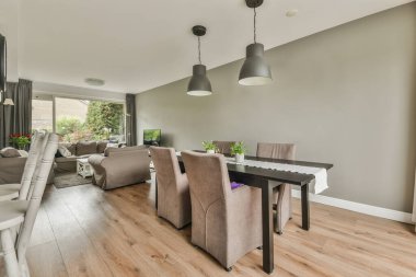 Çağdaş dairenin geniş odasındaki dinlenme odası ve mutfağın yakınındaki sandalyeli ve çiçekli masa.