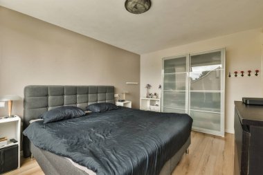 Beyaz çarşaflı rahat bir yatak ve pencerenin yanına lamba konmuş bir komodin ve evdeki aydınlık yatak odasında televizyon.