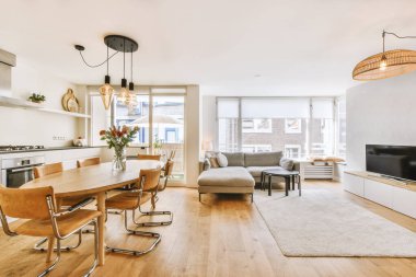 Günümüz minimalist tasarımı. Hafif stüdyo dairesinin ahşap masası ve oturma odası ile beyaz duvarları ve parke zemini arasında yemek masası ve sandalyeleri var.