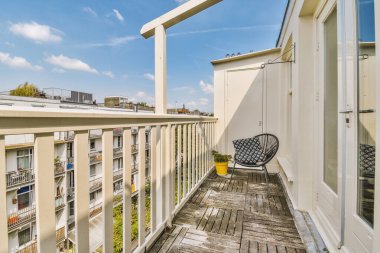 Bright brick balcony with metal railings, wooden chair and door with glass leads to the kitchen