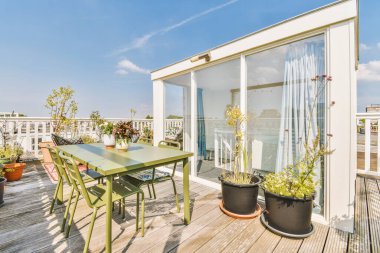 Bright brick balcony with metal railings, wooden chair and door with glass leads to the kitchen