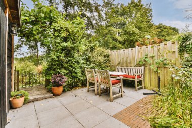 Oturma alanı ve ahşap çitlerin yanındaki küçük bahçesi olan düzgün asfaltlı bir avlu.