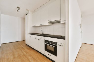 Pencereleri ve ahşap parke zemini olan boş beyaz mutfağın içi.