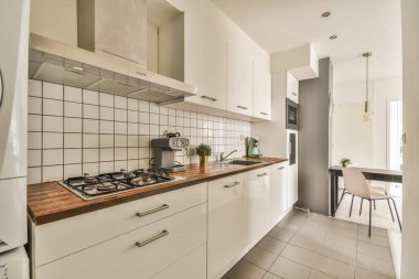 Çağdaş dairenin geniş odasındaki dinlenme odası ve mutfağın yakınındaki sandalyeli ve çiçekli masa.