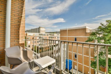 Metal parmaklıklı dar tuğla balkon, tahta sandalye ve camlı kapı mutfağa açılıyor.