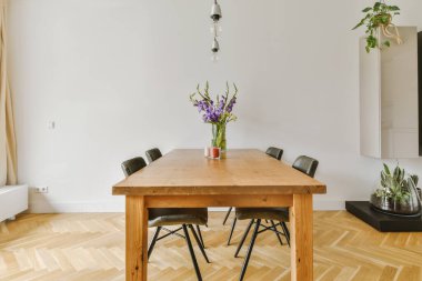 Günümüz minimalist tasarımı. Hafif stüdyo dairesinin ahşap masası ve oturma odası ile beyaz duvarları ve parke zemini arasında yemek masası ve sandalyeleri var.