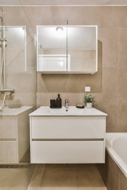 Modern banyoda aynalı lavabo ve cam kapılı duş kutusu ve beyaz fayanslı duvarlar.