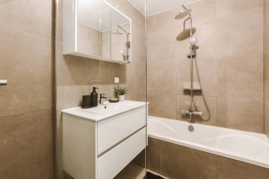 Modern banyoda aynalı lavabo ve cam kapılı duş kutusu ve beyaz fayanslı duvarlar.